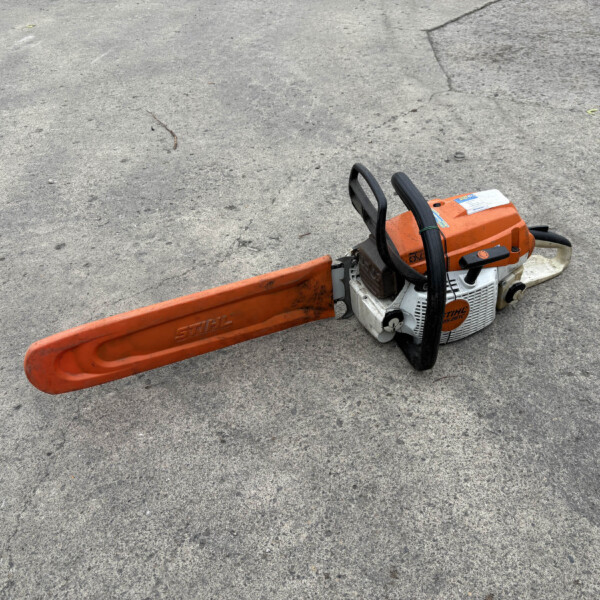 Orange STIHL chainsaw resting on a cracked gray concrete surface with its long orange bar extending across the ground.