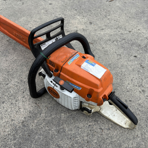 Orange Stihl chainsaw resting on a rough concrete surface, showing the orange bar and black handle up close.