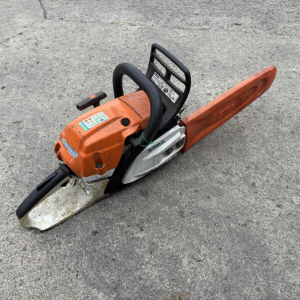 Orange STIHL chainsaw resting on a rough concrete surface, with the guide bar extending to the right and the hand guard visible.