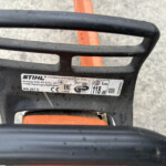 Close-up of a STIHL chainsaw top handle with an orange safety component visible and the model label partially shown on the side.