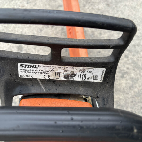 Close-up of a STIHL chainsaw top handle with an orange safety component visible and the model label partially shown on the side.