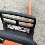 Close-up of a black plastic guard with a Stihl label and orange body, resting on a concrete surface.
