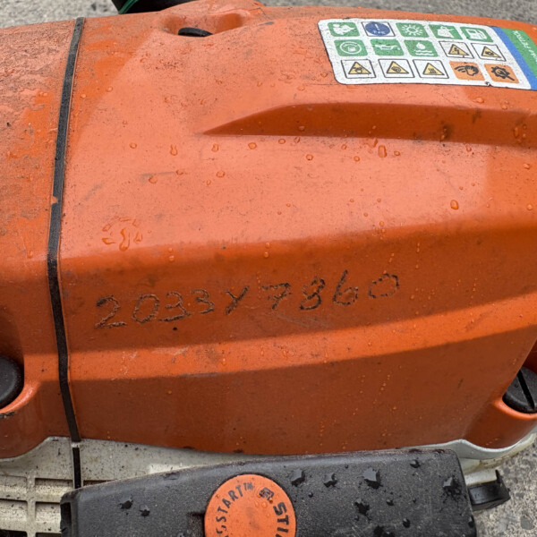 Close-up of an orange power tool body with multiple safety labels and a wet, dirty surface.
