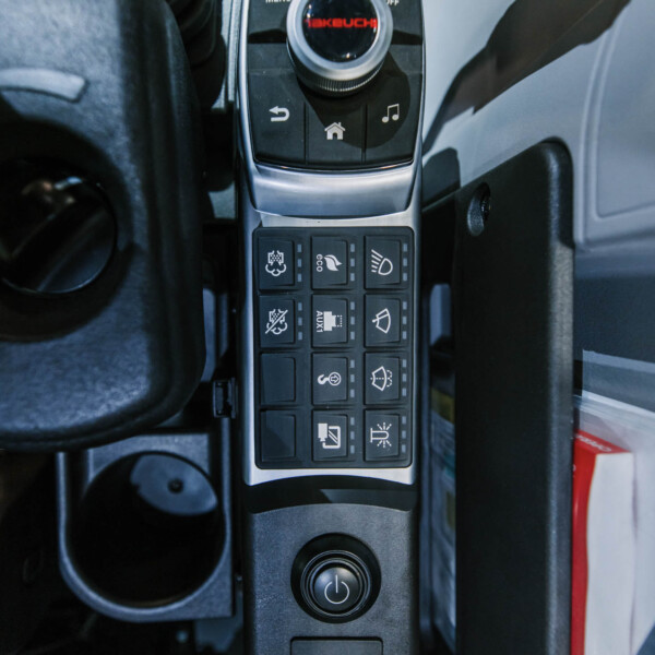 Close-up of a car's center console featuring a circular rotary dial and numerous small square function buttons with icons.
