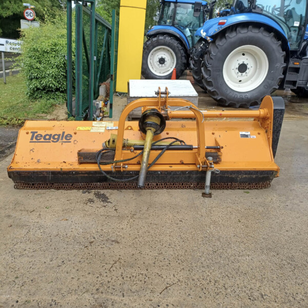 Front view of an orange Teagle mower attachment on a concrete surface with blue tractors in the background.