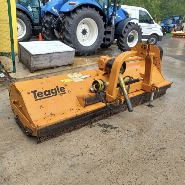 Orange Teagle farm implement in foreground with large tires and a wet concrete yard, blue tractors in background.