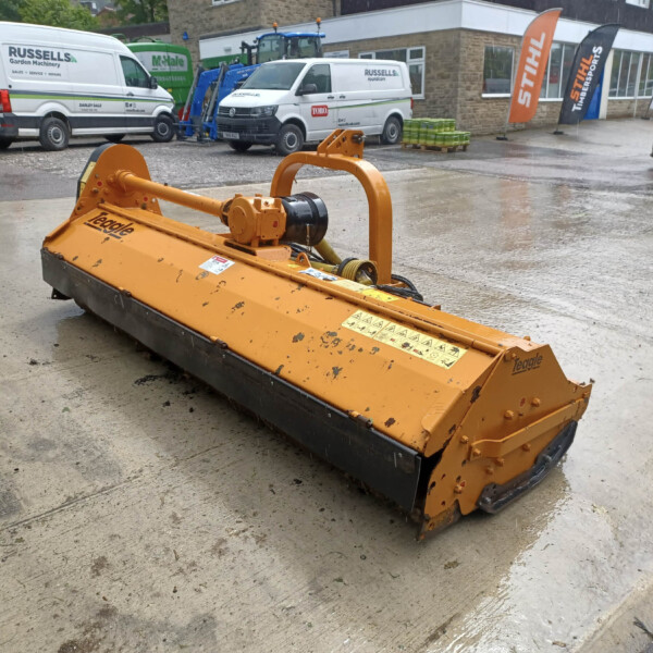 Orange road cutter/soil grinder on a wet concrete surface in a construction yard, with white vans and branded flags visible in the background.