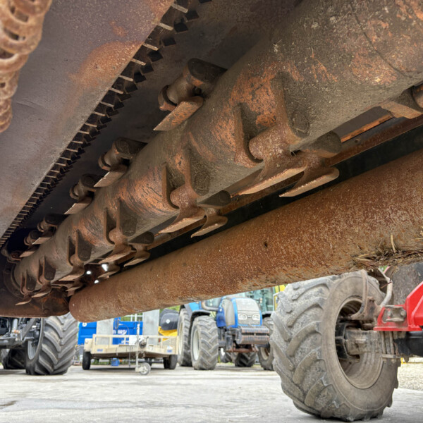 Rusty undercarriage of a large agricultural harvester with worn chains and blades in view