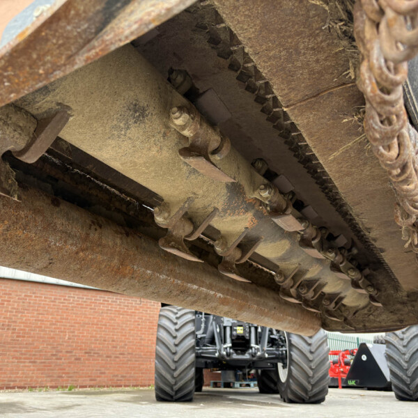 Close-up of a rusty heavy machinery undercarriage with metal tracks and chains showing wear and dirt, under a large orange vehicle.