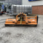 Orange Teagle maintenance machine in the foreground with trailers and farm equipment outside a dealership showroom.