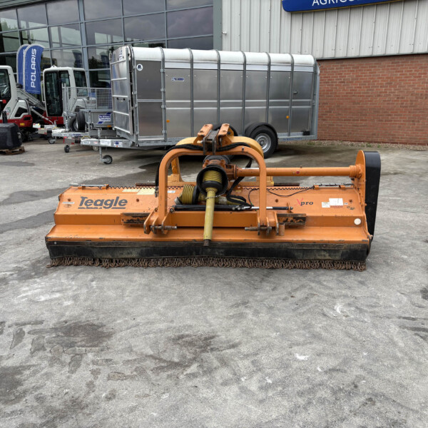 Orange Teagle maintenance machine in the foreground with trailers and farm equipment outside a dealership showroom.