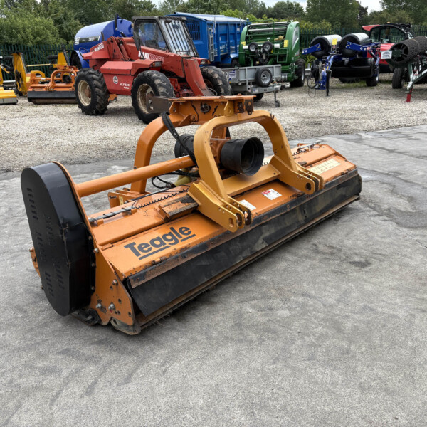 Front view of a large orange Teagle mower attachment in a gravel lot, with various tractors and machinery lined up in the background.