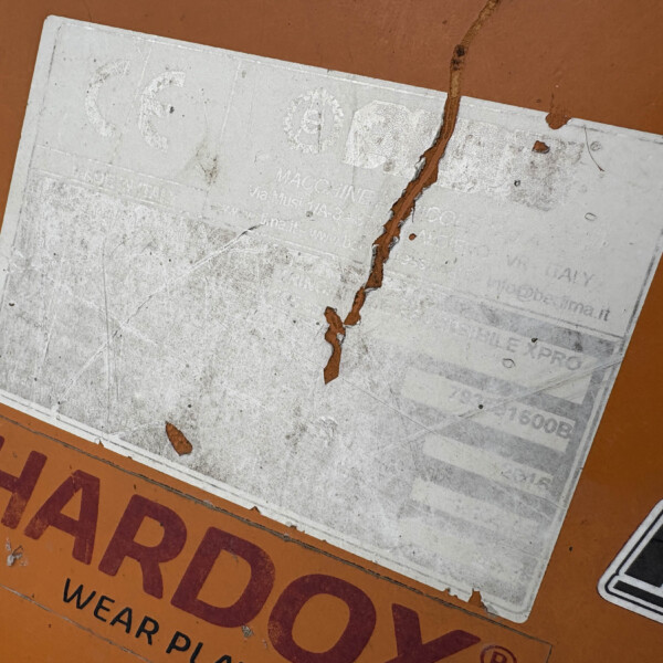Close-up of an orange industrial surface with a worn, peeling white label.
