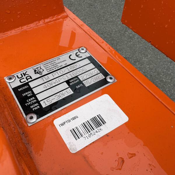 Close-up of an orange metal frame with a data plate showing model, serial number, and barcode information on a wet surface.