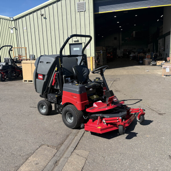 Red ride-on lawn mower with a black seat parked in front of a green corrugated-metal warehouse door.