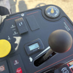 Dashboard of a vehicle with a yellow protective cap, gauge, and control buttons visible; shows hours meter and warning icons in use.