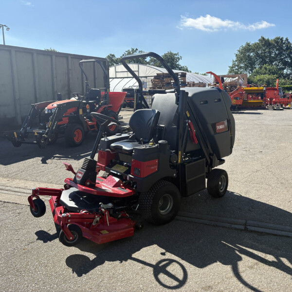 Red agricultural machinery and trailers lined up in an outdoor yard with pallets and a gray storage container under a clear blue sky.