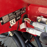 Close-up of a red vehicle interior showing a black serial/label plate, wiring harness, and electrical connectors nearby.