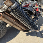 Close-up of rusted metal frame and coiled hydraulic hoses on a heavy truck trailer, with a large treaded tire in the foreground.