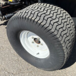 Close-up of a large off-road tire mounted on a heavy vehicle, showing the rugged tread and wheel hub with bolts.