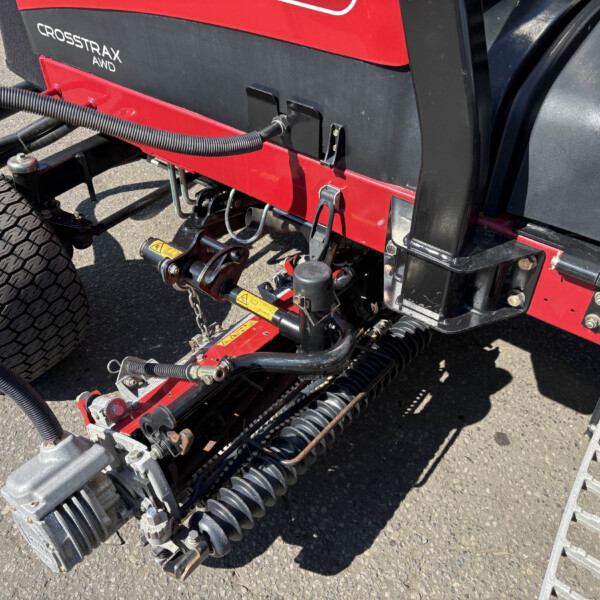 Close-up of a red and black agricultural implement with hoses, chains, and a tire resting on asphalt.