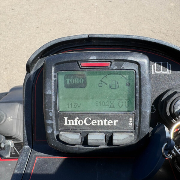 Close-up of a rugged vehicle dashboard showing a green LCD display with the word 'InfoCenter' on the panel and various unreadable readouts, surrounded by a black housing with red trim.