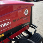 Red Toro Reelmaster 5010-H mower body with logo, hoses, and hydraulic lines visible on a sunny day.