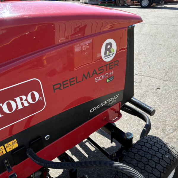 Red Toro Reelmaster 5010-H mower body with logo, hoses, and hydraulic lines visible on a sunny day.