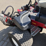 Close-up of a red ride-on mower showing large dual rear tires, a black foot platform, and the operator seat area with exposed machinery nearby.