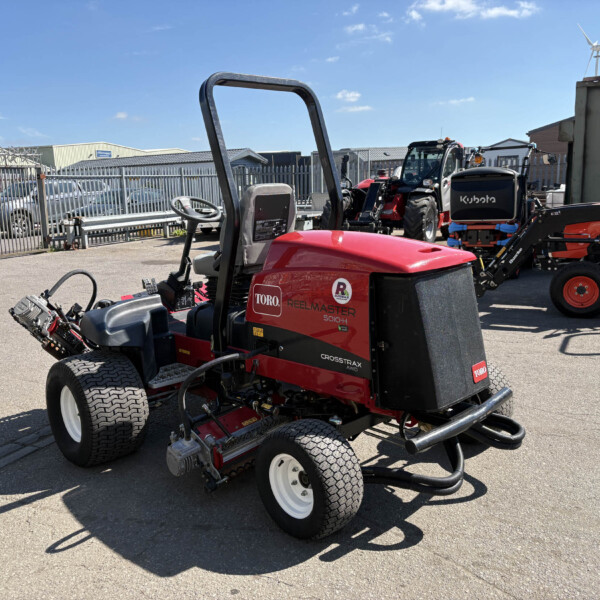 Red Toro riding lawn mower in the foreground, with other machinery and a fence in the background under a blue sky.