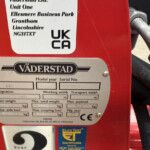 Close-up of a red machine with a metal nameplate showing the Väderstad brand and a smaller label with model/serial information (UK CA) on a red surface.
