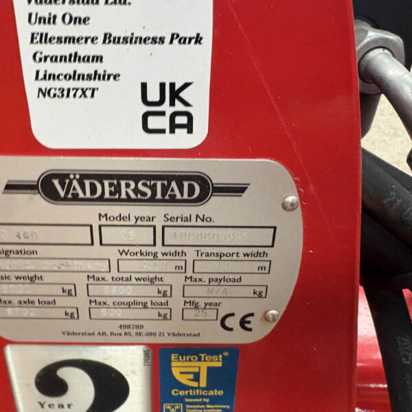 Close-up of a red machine with a metal nameplate showing the Väderstad brand and a smaller label with model/serial information (UK CA) on a red surface.