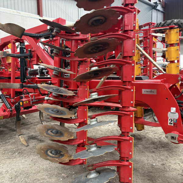 Red multi-disc cultivator with rusted round discs mounted on a sturdy frame inside a storage area.