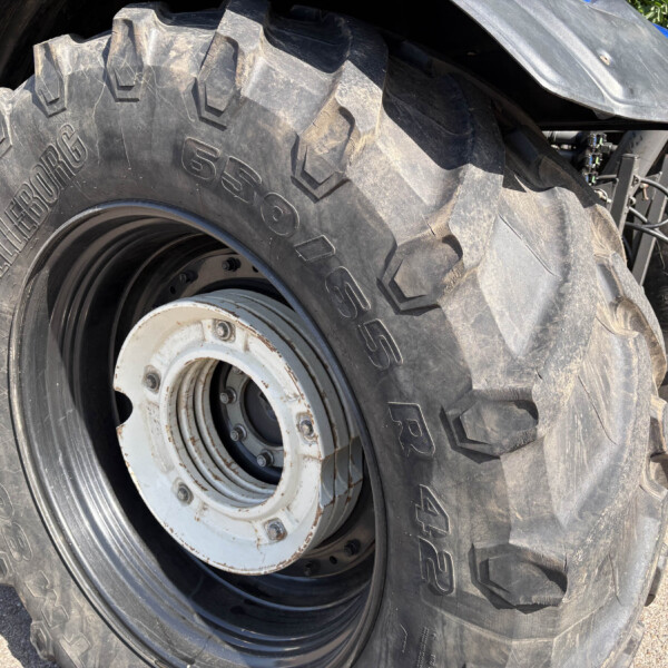 Close-up of a large agricultural tractor tire with deep, aggressive tread and a white metal rim