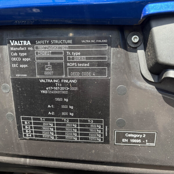 Close-up of a black data plate on a blue vehicle showing Valtra safety structure details and weight specifications.