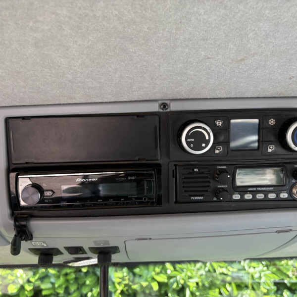 Dashboard center console with climate control knobs and a Pioneer stereo, in a grey interior with a windshield view of greenery outside.