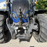 Front view of a blue agricultural tractor showing oversized rear tires, front hitch, and dashboard area between the tires.