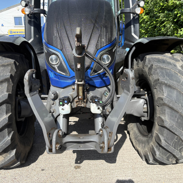 Front view of a blue agricultural tractor showing oversized rear tires, front hitch, and dashboard area between the tires.