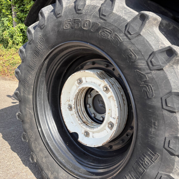 Close-up of a large tractor tire with deep treads and a white, rusted rim.