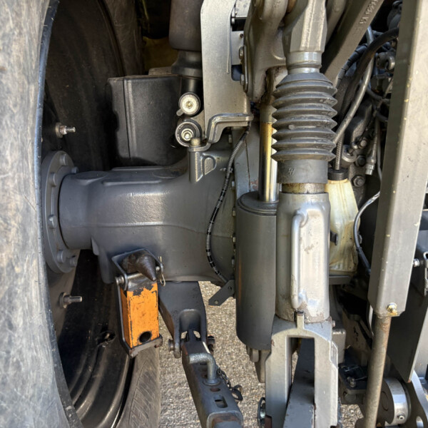 Close-up of a heavy machinery undercarriage showing a hydraulic hose, a bellows boot, and metal linkages near a large tire.