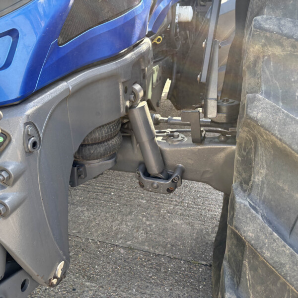 Close-up of a blue tractor chassis showing hydraulic components, hitch, and a large tire nearby.