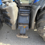 Close-up of a tractor cab foot pedals and steps between large front tires.