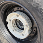 Close-up of a large tire with a rusted white wheel hub and visible lug nuts.