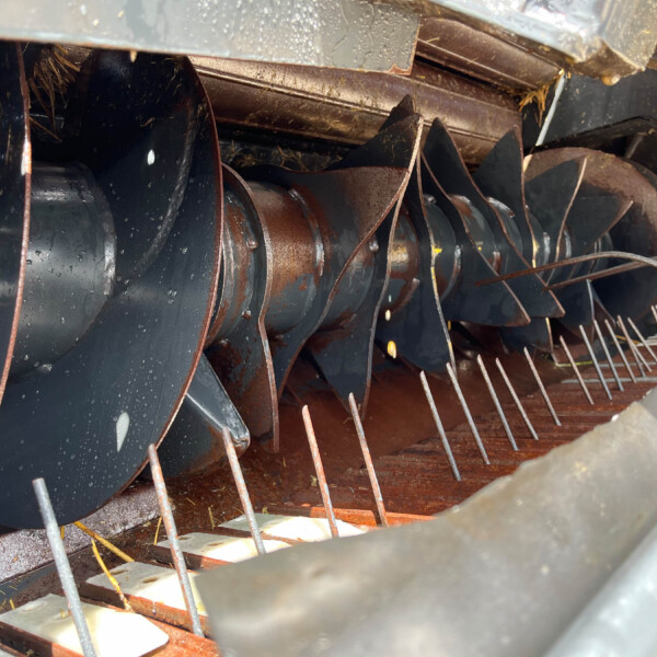 Close-up of a rusted, curved metal blade assembly inside a dark metal housing, with wet surfaces and several thin rods crossing the scene.