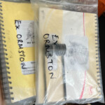 Plastic zip-top bag holding printed manuals and diagrams laid over a yellow spiral notebook; visible sketches and text on the papers.