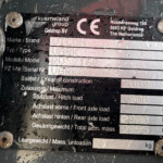 Weathered metal equipment identification plate with brand name, address, and weight fields, partially obscured by dirt and rust.