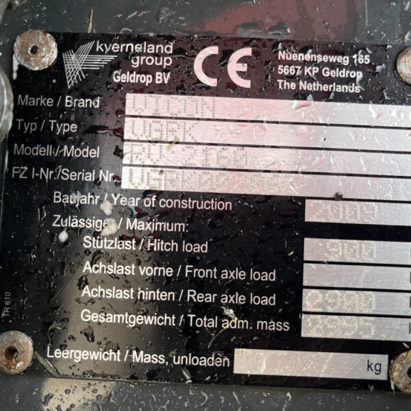 Weathered metal equipment identification plate with brand name, address, and weight fields, partially obscured by dirt and rust.