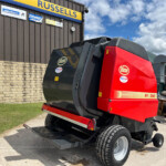 Red Vicom combine harvester outdoors beside a brick wall and a building with a yellow-and-blue Russell sign and logos in the background.