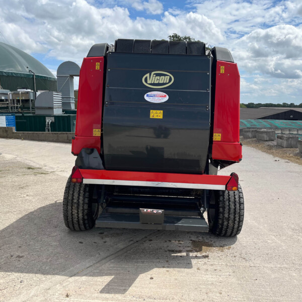 Rear view of a blue and red Vicon industrial machine on a trailer in an outdoor construction yard with a blue sky and clouds behind.