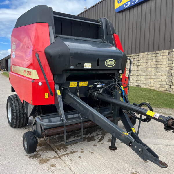 Red and dark gray Vicon header attachment for a combine harvester parked outside a farm supply yard building.